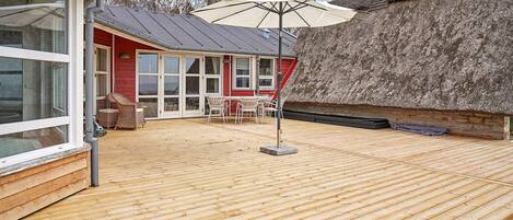 A wooden deck with a thatched roof structure, a dining area with chairs, and a large umbrella.
