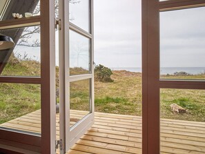 A wooden deck with a glass door leading to a grassy area with a view of the sea. - 4 Star Holiday Home in Aakirkeby (Akirkeby)
