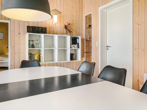 A room with a dining table, chairs, a white shelving unit, and a door. - 4 Star Holiday Home in Aakirkeby (Akirkeby)