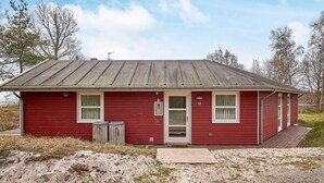 A red single-story building with a metal roof, a front door, and two windows. - 4 Star Holiday Home in Aakirkeby (Akirkeby)