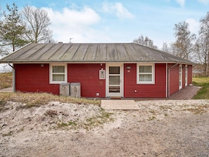 A red single-story building with a metal roof, a front door, and two windows. - 4 Star Holiday Home in Aakirkeby (Akirkeby)