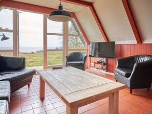 A modern living room with a wooden table, leather chairs, a television, and large windows offering a view of the outdoors. - 4 Star Holiday Home in Aakirkeby (Akirkeby)