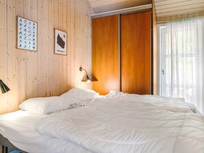 A bedroom with a bed, a wall-mounted lamp, and a wooden door. - 4 Star Holiday Home in Aakirkeby (Akirkeby)