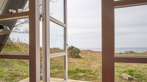 A wooden deck with a glass door leading to a grassy area with a view of the sea. - 4 Star Holiday Home in Aakirkeby (Akirkeby)