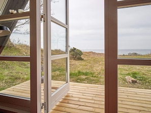 A wooden deck with a glass door leading to a grassy area with a view of the sea. - 4 Star Holiday Home in Aakirkeby (Akirkeby)