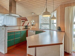 A kitchen with wooden cabinets, a built-in dishwasher, and a large island with a countertop. - 4 Star Holiday Home in Aakirkeby (Akirkeby)