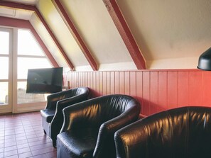 A room with a sloped ceiling, a television mounted on the wall, and several leather chairs arranged for seating. - 4 Star Holiday Home in Aakirkeby (Akirkeby)
