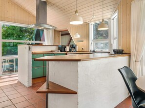 A kitchen with a central island, green cabinets, a window, and a dining area with a chair. - 4 Star Holiday Home in Aakirkeby (Akirkeby)