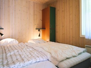 A room with wooden walls, a bed with a quilt, a green wardrobe, and a wall-mounted lamp. - 4 Star Holiday Home in Aakirkeby (Akirkeby)