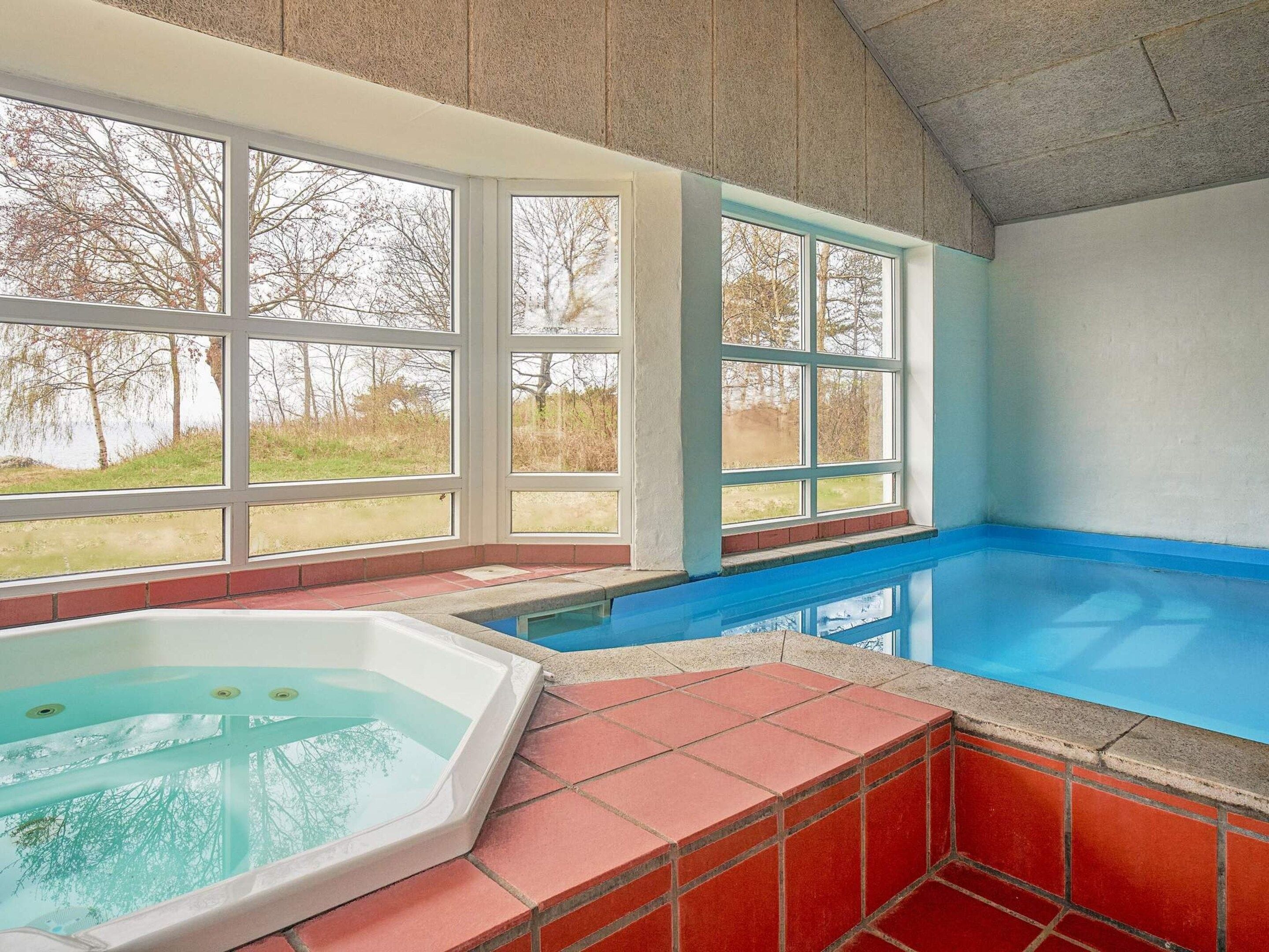 A swimming pool with a hot tub, large windows, and a view of trees.