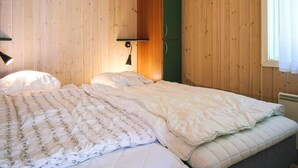 A room with wooden walls, a bed with a floral-patterned duvet, a green wardrobe, and a wall-mounted lamp. - 4 Star Holiday Home in Aakirkeby (Akirkeby)