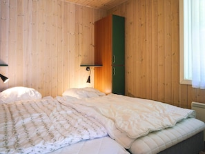 A room with wooden walls, a bed with a floral-patterned duvet, a green wardrobe, and a wall-mounted lamp. - 4 Star Holiday Home in Aakirkeby (Akirkeby)