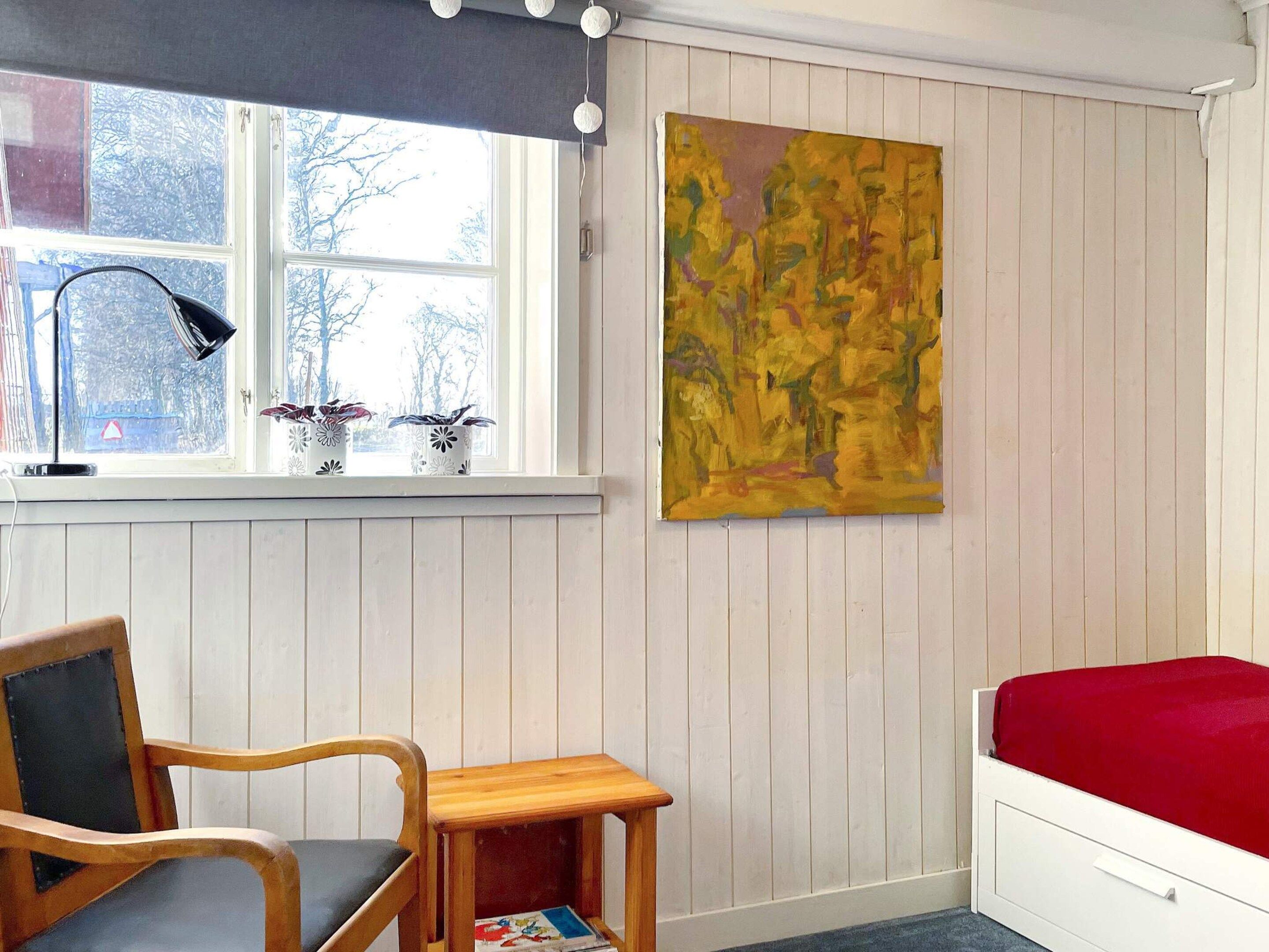 A room with a bed, a desk, a chair, a window with blinds, a lamp, and a painting.