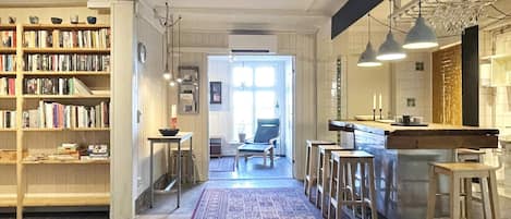 A spacious interior with a central hallway, a kitchen area with bar stools, and a bookshelf filled with books.