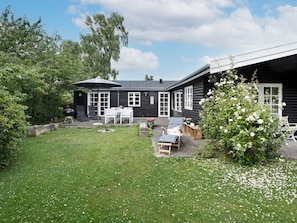 Ett svart trähus med en uteplats, en grill och utomhusmöbler.
