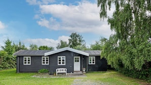 A black wooden house with a white door and windows, a bench, and a gravel path leading to the entrance. - 4 Person Holiday Home in Helsinge (Helsinge)