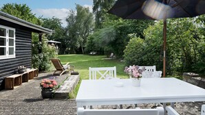 A patio with a white table and chairs, a wooden bench, and a garden with a lawn and trees. - 4 Person Holiday Home in Helsinge (Helsinge)