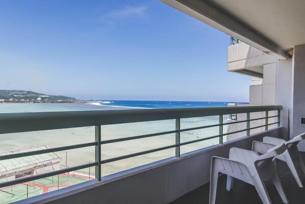 A balcony with a view of the beach and ocean. There are white plastic chairs and a railing. - Alupang Beach Tower, UPGRADED units (Tamuning)