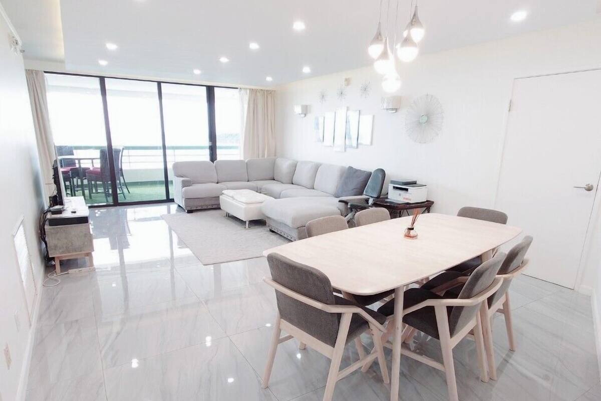 Una sala moderna con un amplio sofá modular, una mesa de comedor con sillas y vistas a un balcón exterior a través de puertas corredizas de vidrio.