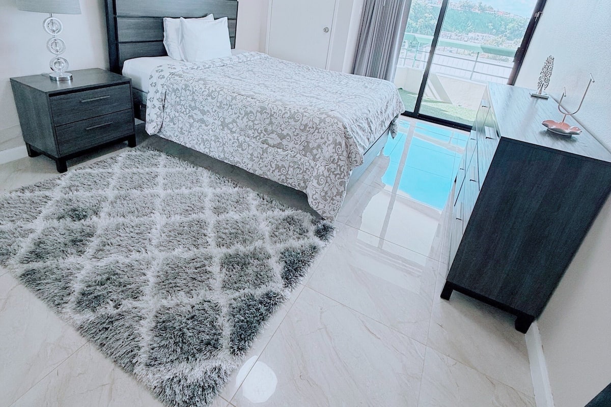 Un dormitorio con cama, mesita de noche, cómoda, alfombra y vistas a una piscina.