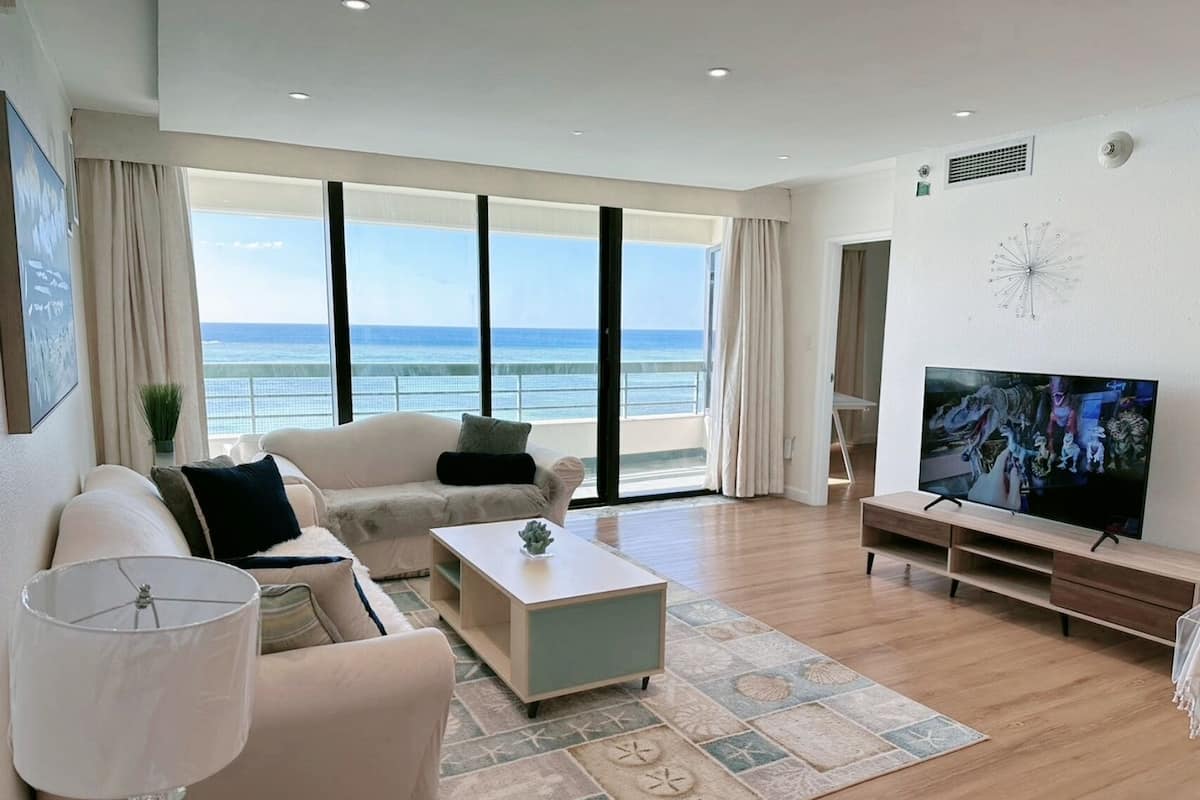 Una sala de estar moderna con un televisor grande, asientos cómodos y vista al océano.
