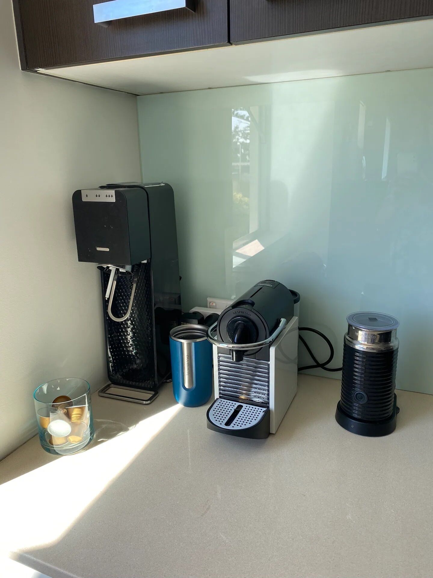 Une petite cuisine équipée d’une machine à café, d’une bouilloire, d’une tasse et d’un thermos, le tout posé sur le comptoir.