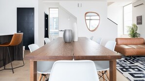 Ett modernt matområde med ett träbord, vita stolar, en brun lädersoffa och en svartvit mönstrad matta.
