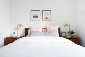 Quarto bem arrumado com uma cama grande, duas mesas de cabeceira e quadros nas paredes.