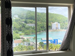 A view from a window with patterned curtains, overlooking a coastal area with buildings, a dock, and a clear blue sea. - Turtle Beach Towers Vacation  (Ocho Rios)