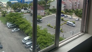Udsigt fra et vindue over et kystområde med bygninger, en parkeringsplads og et vandareal.