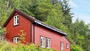 A red wooden house with a gabled roof, surrounded by dense green foliage. - 4 Person Holiday Home in Hardbakke (Solund)