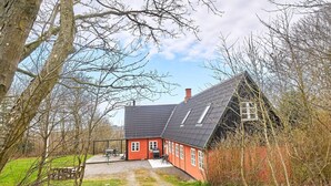 Een rode woning met een schuin dak en schoorsteen, omgeven door bomen en een grindpad.