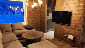 Une pièce confortable avec une grande fenêtre, un téléviseur à écran plat, un canapé, une petite table et un mur en bois.