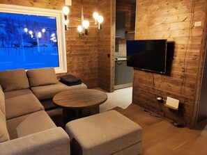 A cozy room with a large window, a flat-screen TV, a sofa, a small table, and a wooden wall. - 4 Star Holiday Home in Idre (Idre)