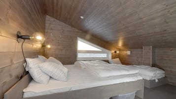 Un dormitorio con techo inclinado, paredes de madera, cama con ropa blanca, tragaluz y luces fijadas a la pared.