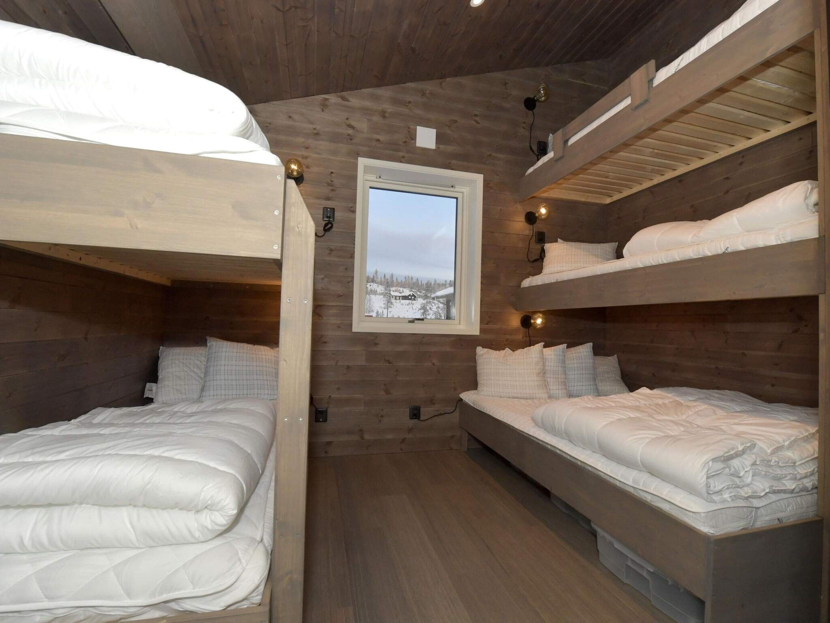 Habitación pequeña con literas, paredes de madera, ventana con vistas a un paisaje nevado y luces fijadas a la pared.