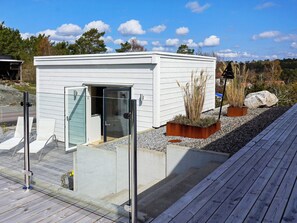 A small, white, single-story building with a glass door and a sliding door, surrounded by a wooden deck and gravel. - 2 Person Holiday Home in Marstrand (Marstrand)