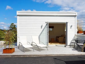 Un bâtiment moderne, de plain-pied, avec une façade blanche, une entrée dotée d’une porte-fenêtre coulissante et un patio aménagé avec du mobilier d’extérieur.