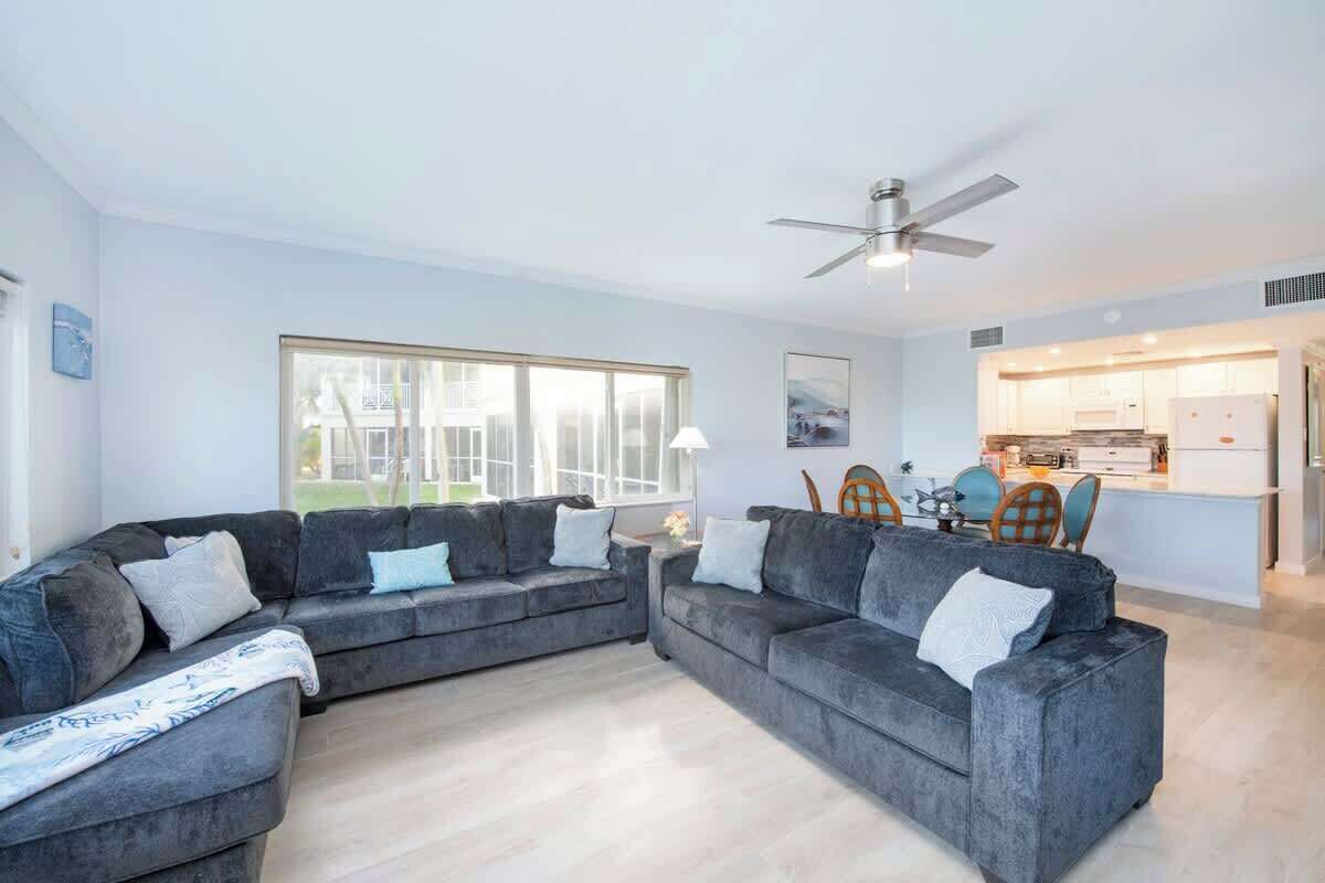 A modern living room with a sectional sofa, a dining area with a table and chairs, and a kitchen in the background.