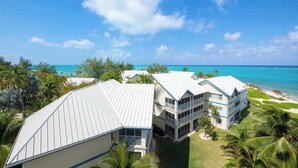 Un hotel frente a la playa con varias construcciones, cielo azul despejado y vista al océano.