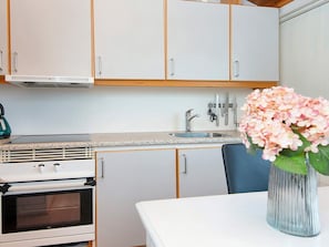 A kitchen with white cabinets, a stainless steel sink, a stove, and a vase with flowers on the table.