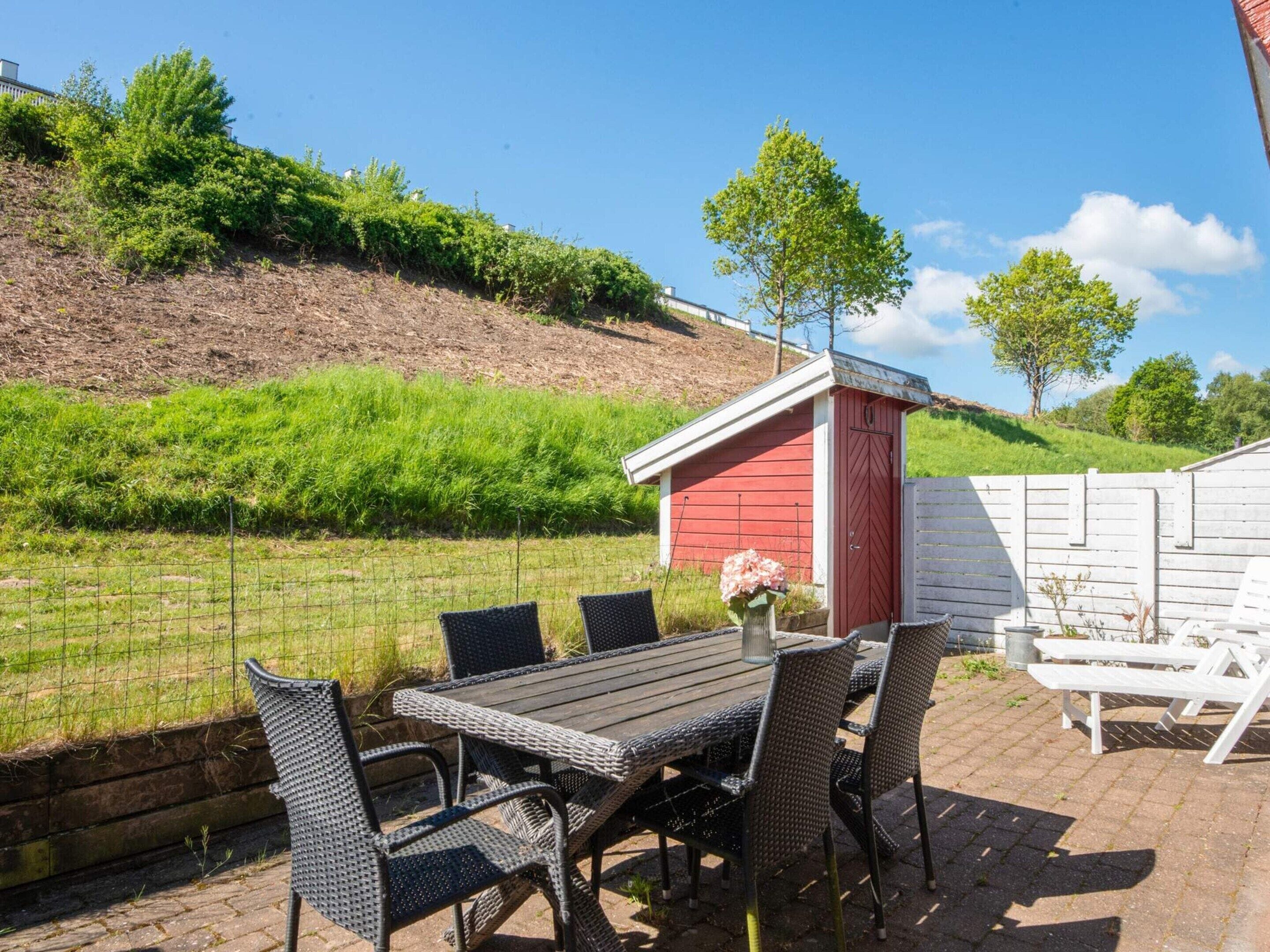 Eine Terrasse mit Tisch und Stühlen, ein rotes Gartenhaus und ein weißer Zaun.