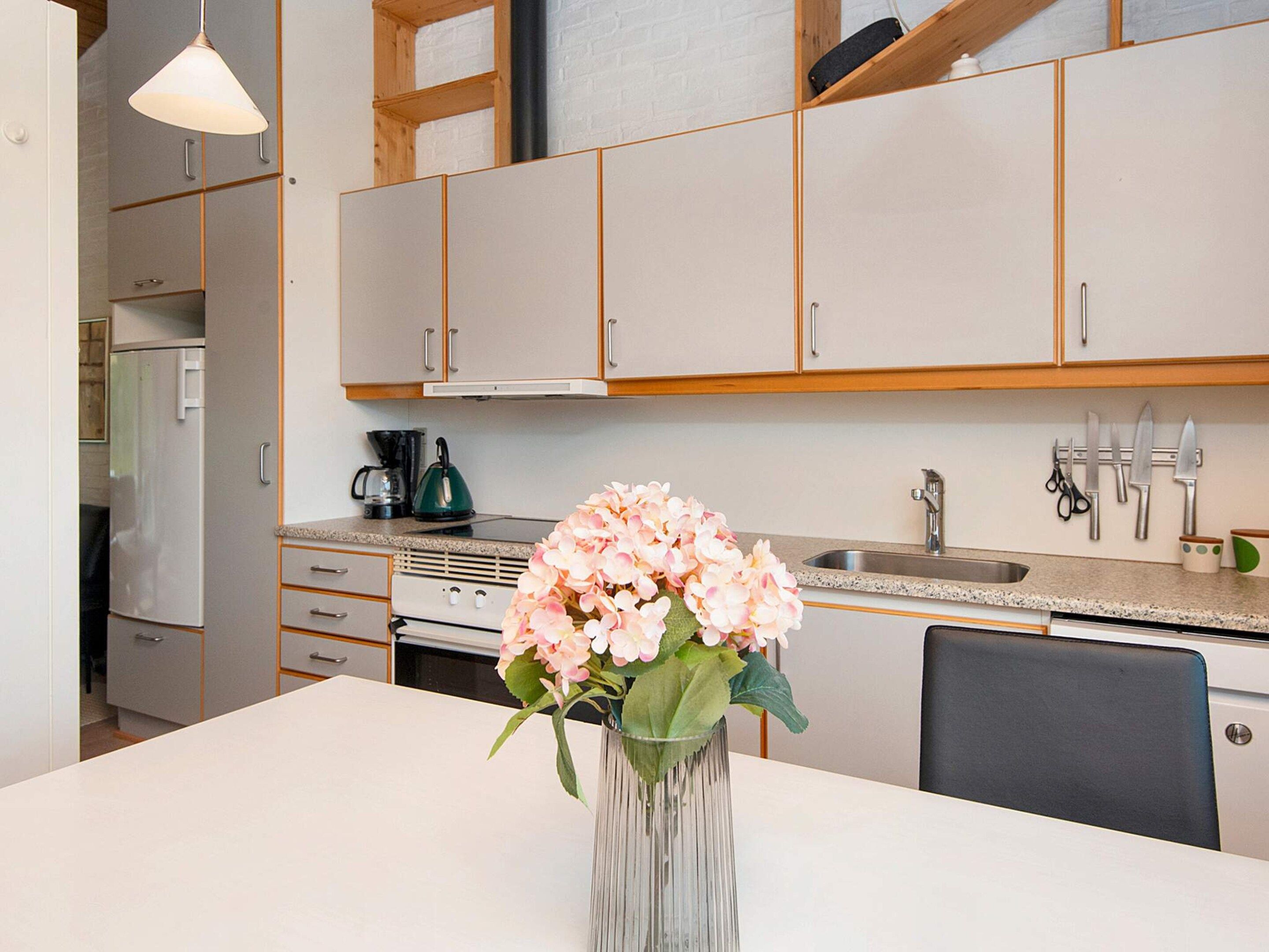 Une cuisine moderne avec des meubles blancs, un évier en acier inoxydable et un vase rempli de fleurs posé sur le plan de travail.