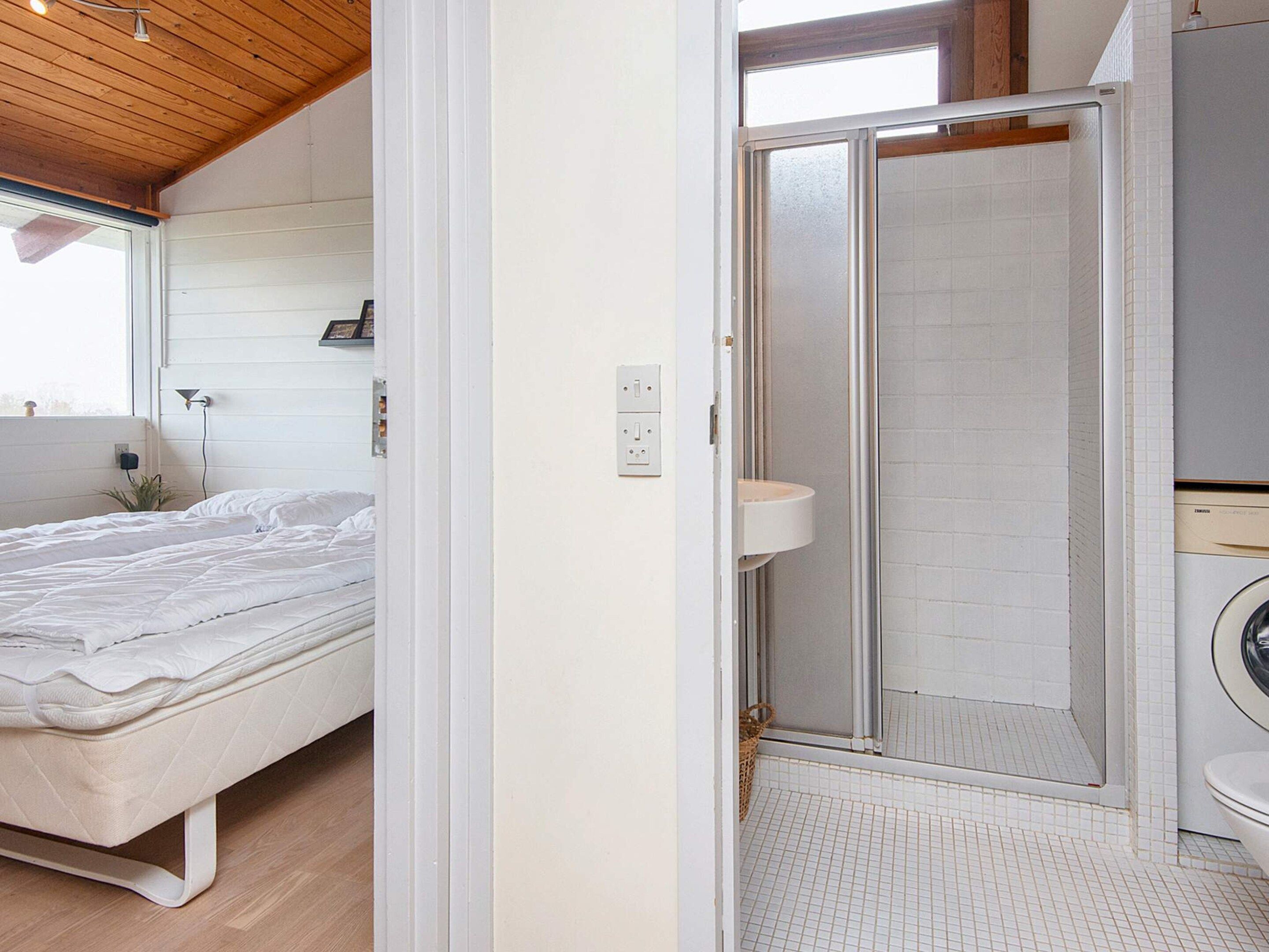 Un dormitorio con cama, ducha de mampara y lavadora.