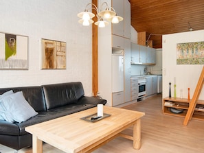 A modern kitchen with white cabinets, a wooden ceiling, and a dining area with a black leather sofa and a wooden coffee table. - 5 Person Holiday Home in Aabenraa (Aabenraa)