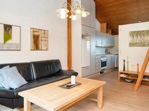 A modern living space with a black leather sofa, a wooden coffee table, and a kitchen area with white cabinets and a wooden ceiling.
