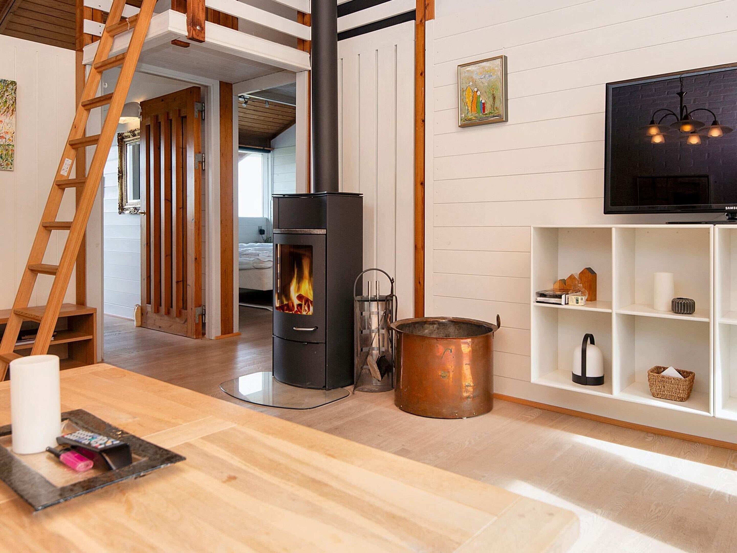 A modern living room with a wood-burning stove, a television, and a ladder.