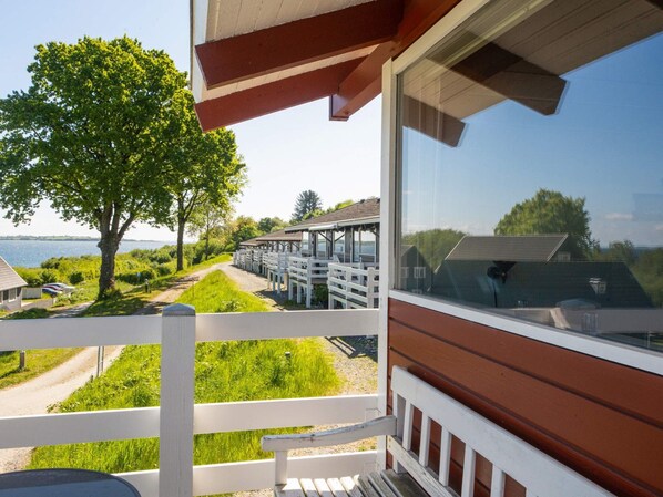 A balcony with a view of a lake, a wooden deck, and a white fence.