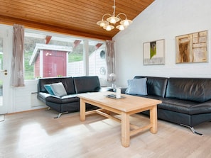 Uma sala de estar moderna com teto de madeira, dois sofás de couro preto, uma mesa de centro de madeira e uma janela grande com cortinas.