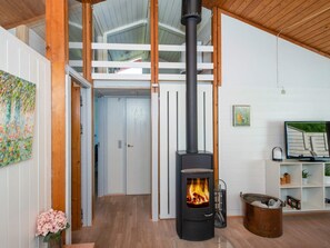 A room with a wood-burning stove, wooden beams, a white door, and a shelf with items. - 5 Person Holiday Home in Aabenraa (Aabenraa)
